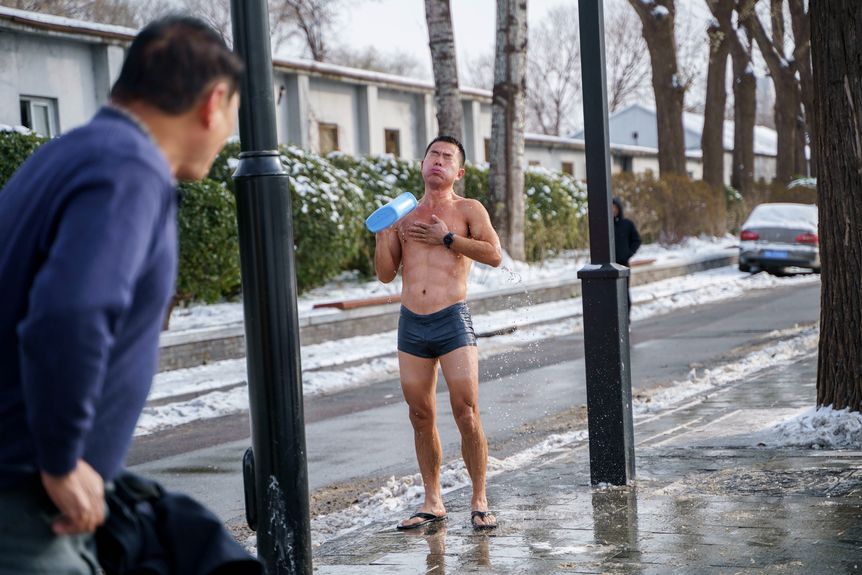 A man in swimwear standing on a street, First snow in Beijing in 2023