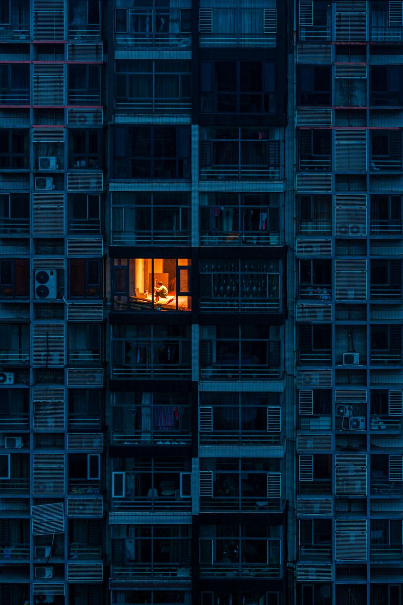 A lit window at night in Li Xiao’s hometown, Wu’an in Hebei province, Beijing’s apartment buildings on camera