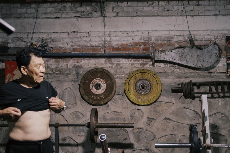 Li Shulin lifts up his T-shirt to cool off after working out. On the wall behind him is the halberd won by Zhang Wei, the founder of Erqi Gym.