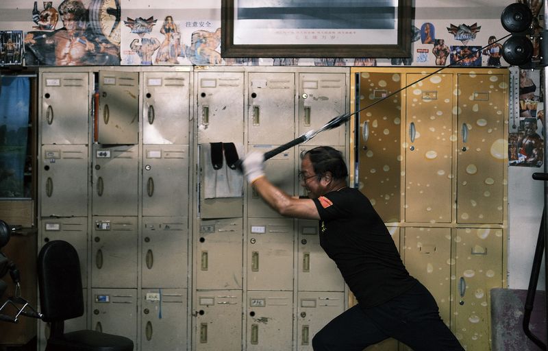 Mi Wenyuan, 62, does a tricep workout by the lockers, where pictures of sports figures hang