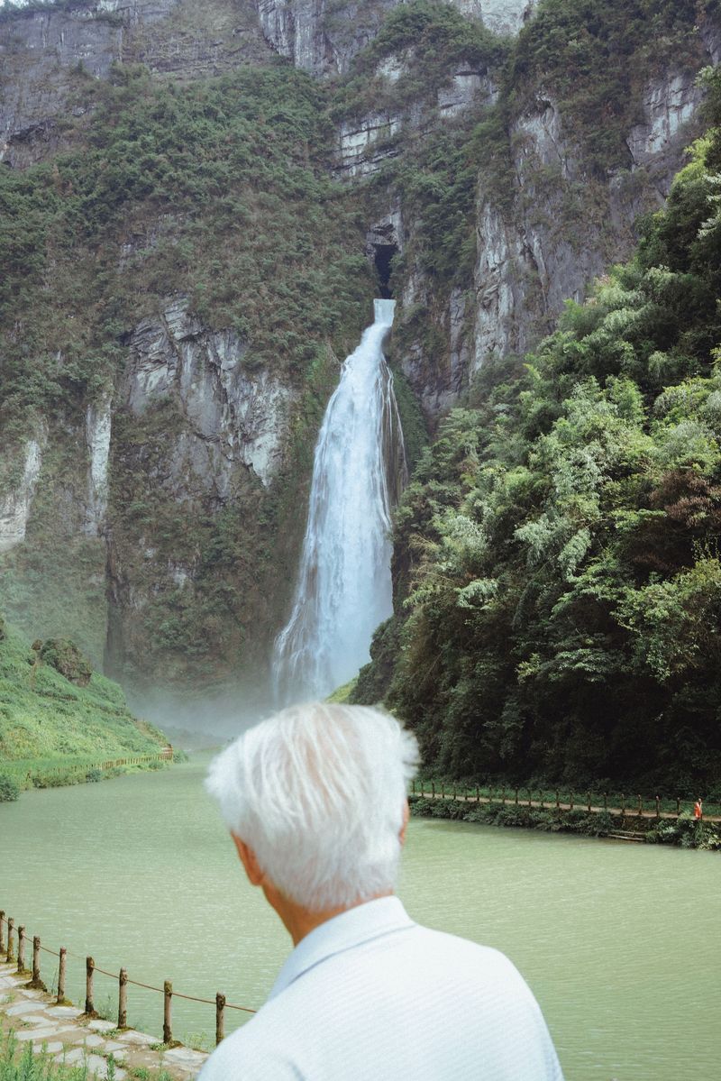A man looking at a waterfall coming out from a cave halfway up the mountain in west Hunan province
