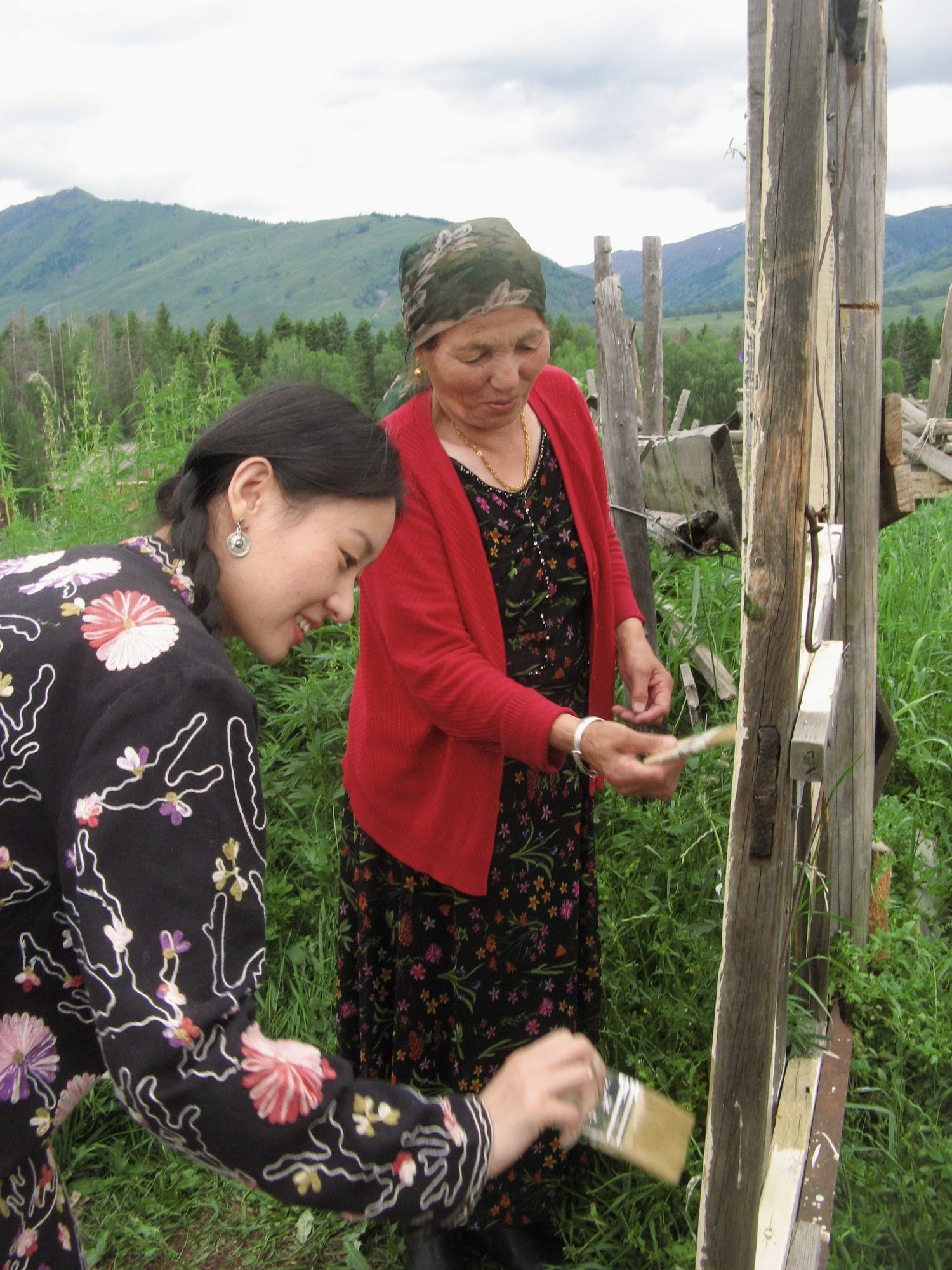 A visitor helps Apa paint her fence in Altay, Xinjiang