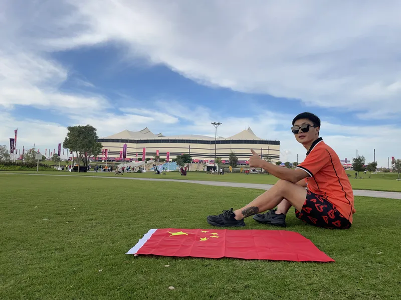 A Chinese soccer fan sitting on a lawn with the Chinese flag