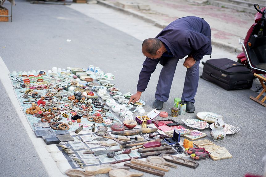 An antique seller arranges his products, including old coins, beads, incense burners, and books