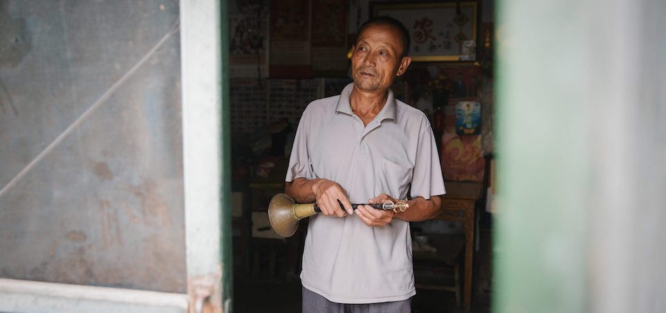 An old Chinese man holds his suona as he looks out a window