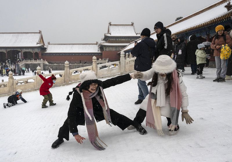 People in winter clothing joyfully playing in the snow in Palace Museum