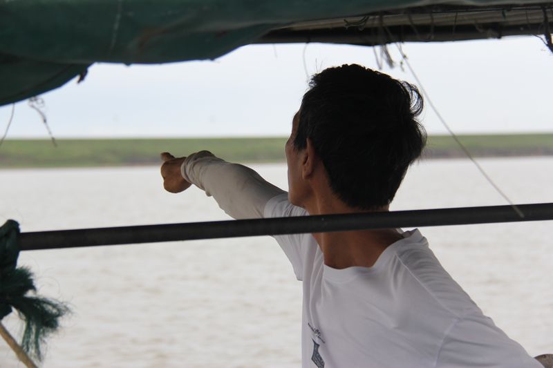 A fisherman points into the distance atop a boat on Poyang Lake