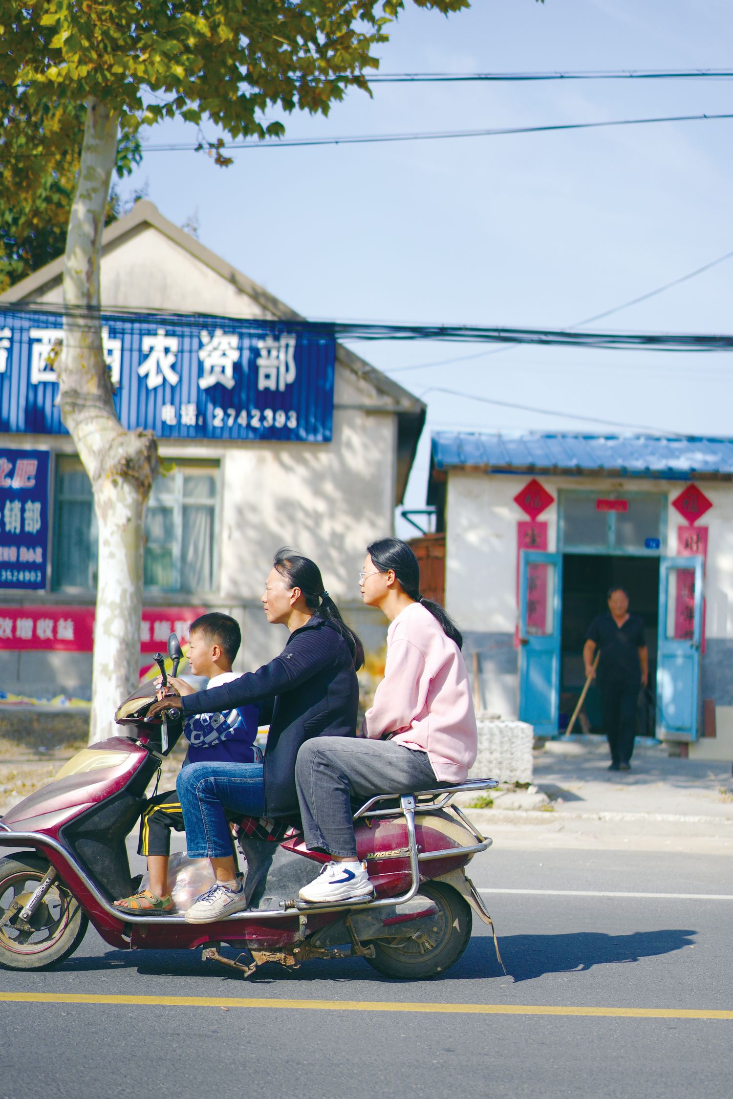 A group of three people ride a red electric scooter