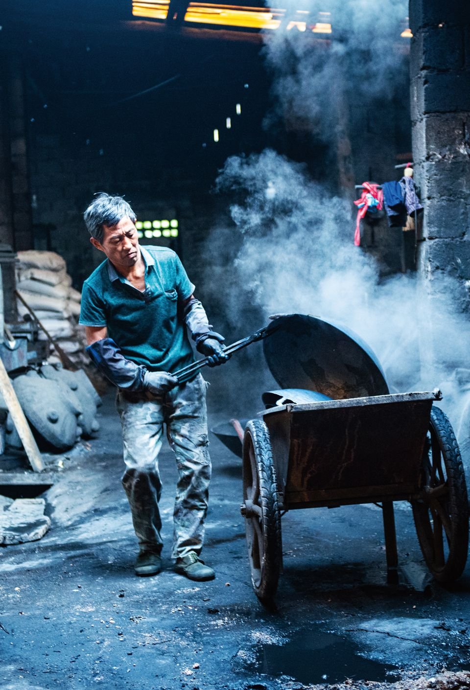 An employee cools down a newly fashioned Chinese wok, Molding a Chinese wok