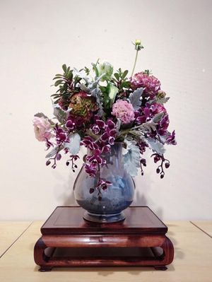 Chinese flower arrangement in round white flower vase on wooden base