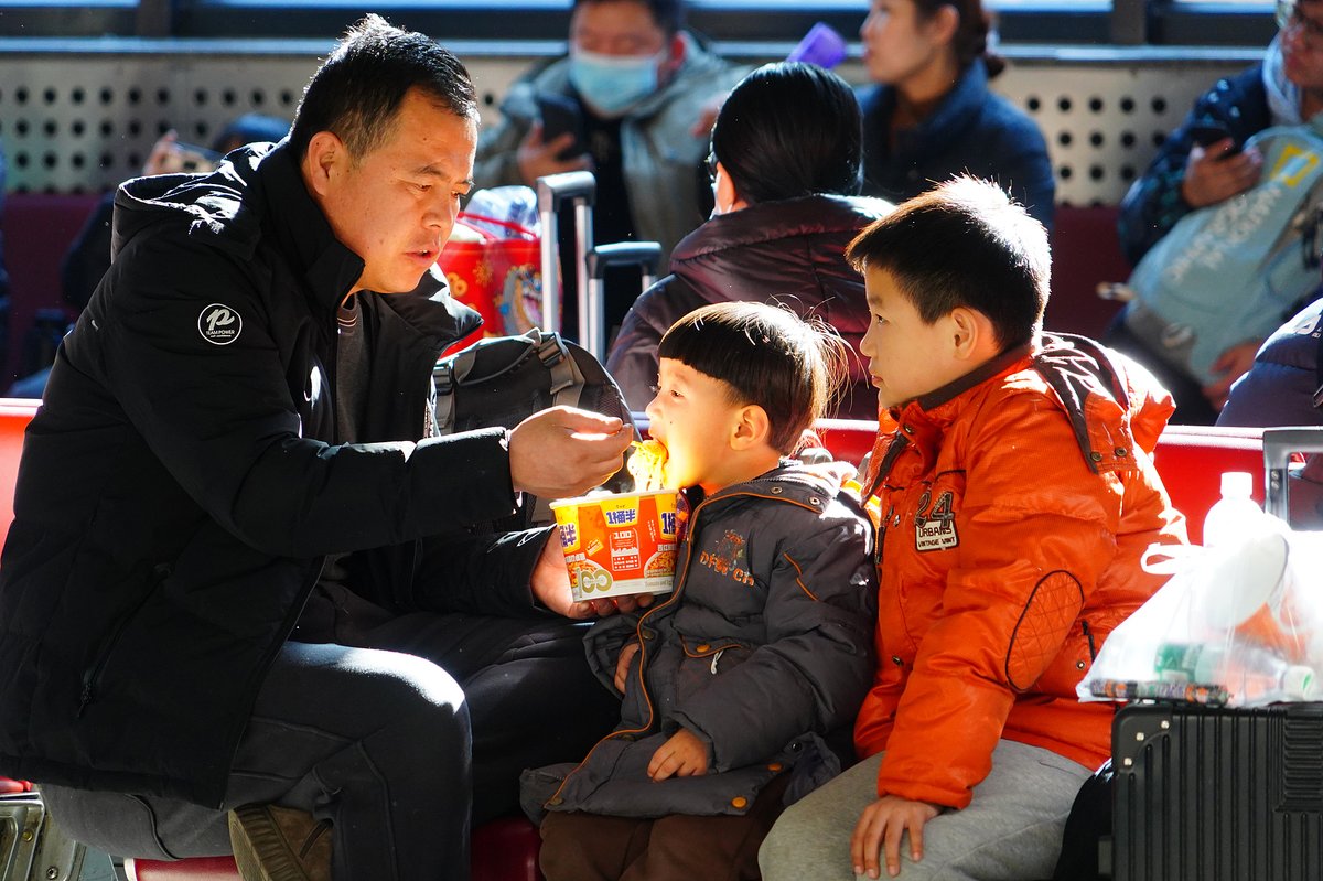 A Chinese father feeds his two sons instant noodles during the Spring Festival rush in 2024