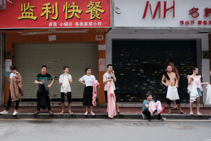 The recruitment process in Kanglu. The employers stand by the roadside, holding sample products and a cardboard sign with the desired skills they seek and prices.