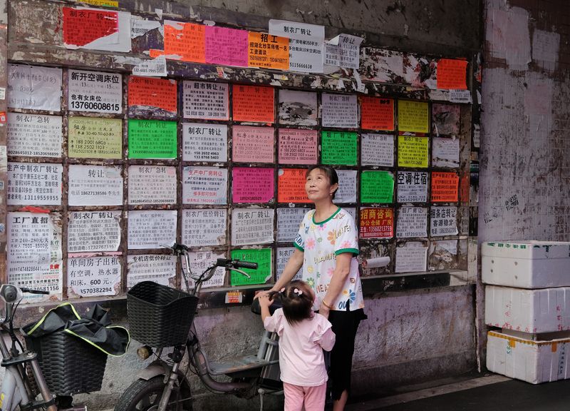 A woman and a girl stand in front of a bulletin board wallpapered with flyers for transferring factories in Lujiang village, Guangzhou, June 10, 2023.