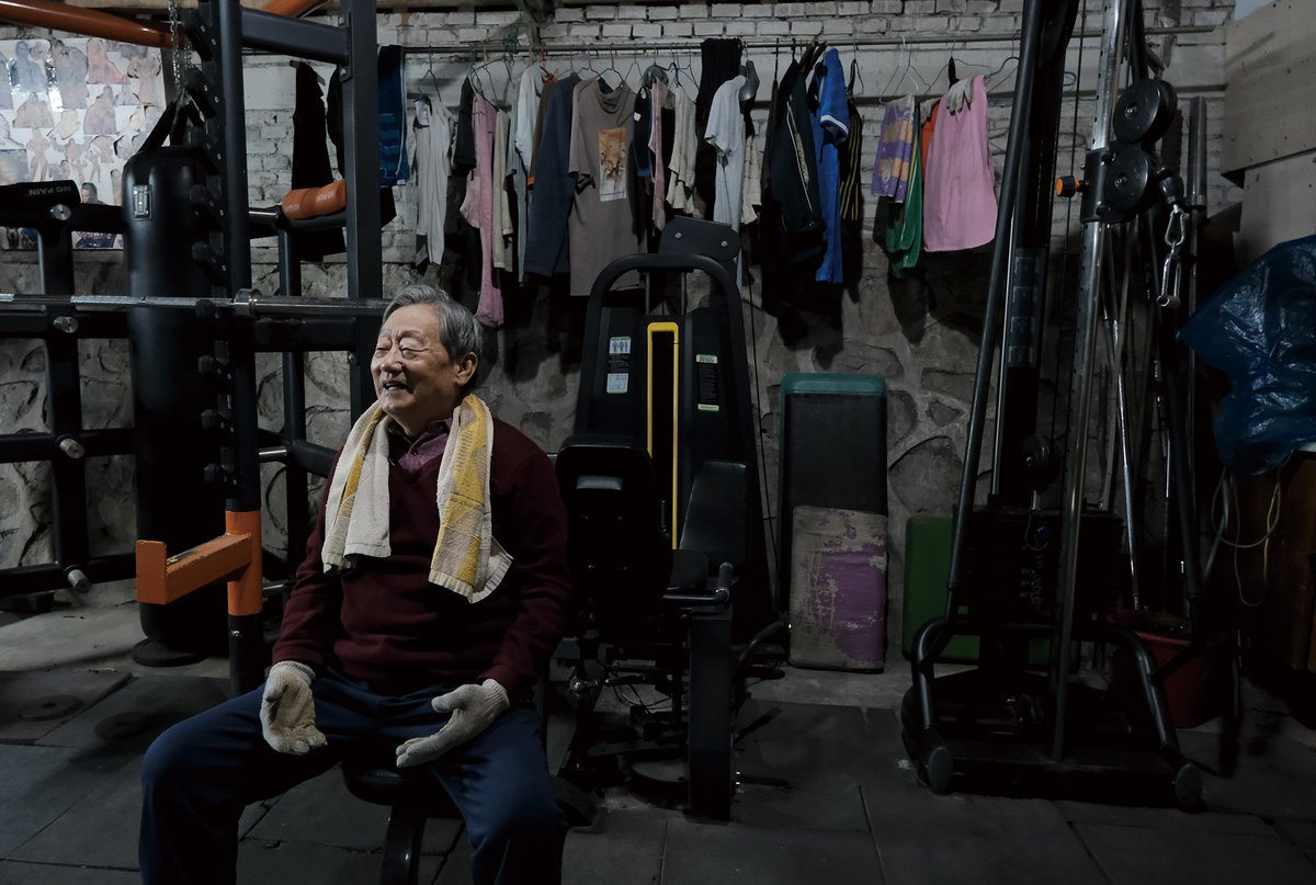 Yang Hongzeng smiles as he talks to other gym members in between workouts. Behind him are the clothes that members have hung out to dry.