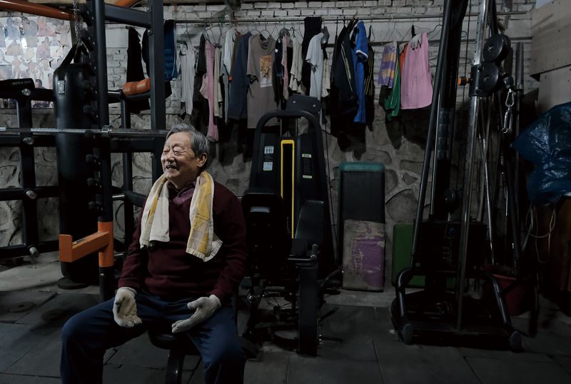 Yang Hongzeng smiles as he talks to other gym members in between workouts. Behind him are the clothes that members have hung out to dry.