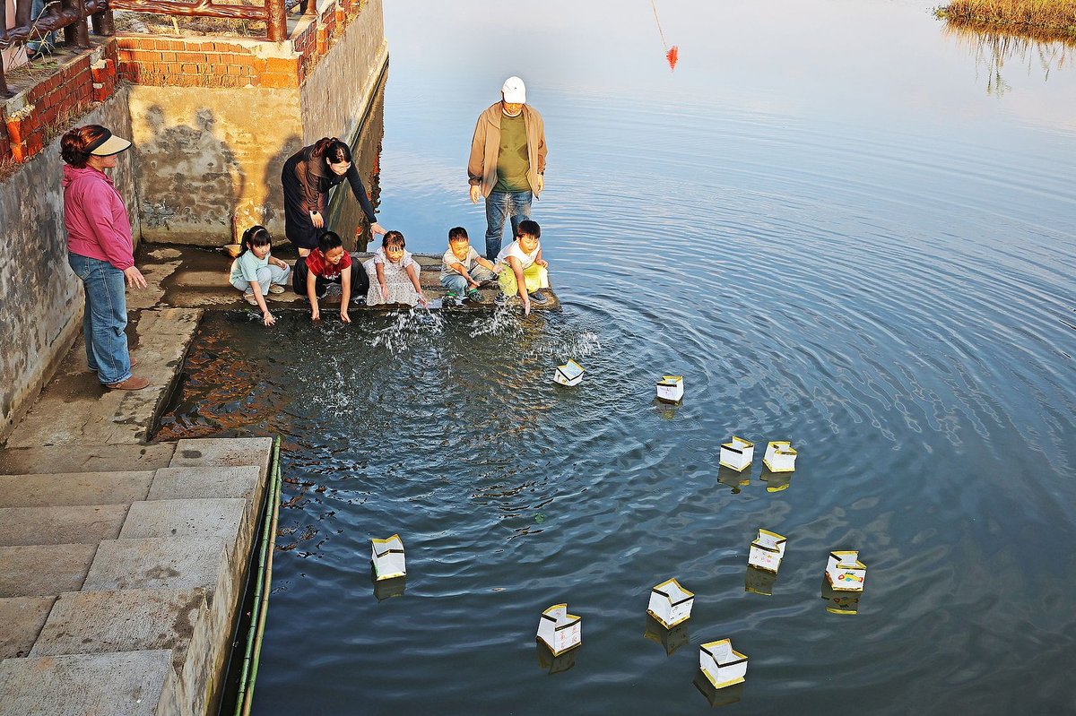 a group of children releases handmade boats on the river on the night of Qixi,