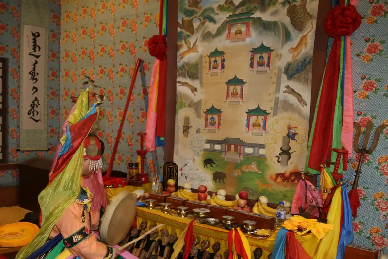 a shaman beats a drum in front of pictures of gods during a ritual, keeping shamanism alive in china