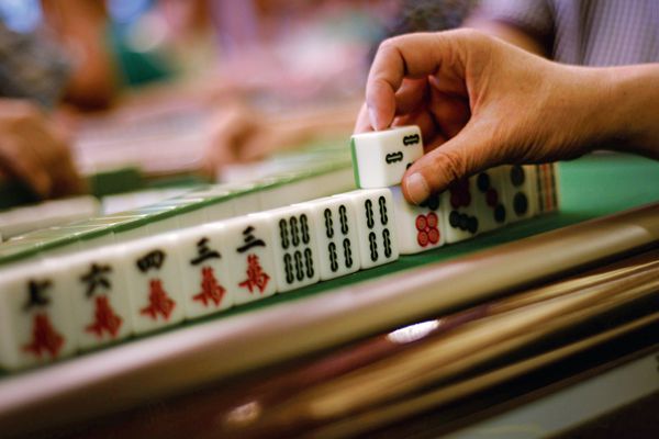 A hand putting a mahjong tile into place during a mahjong match. 