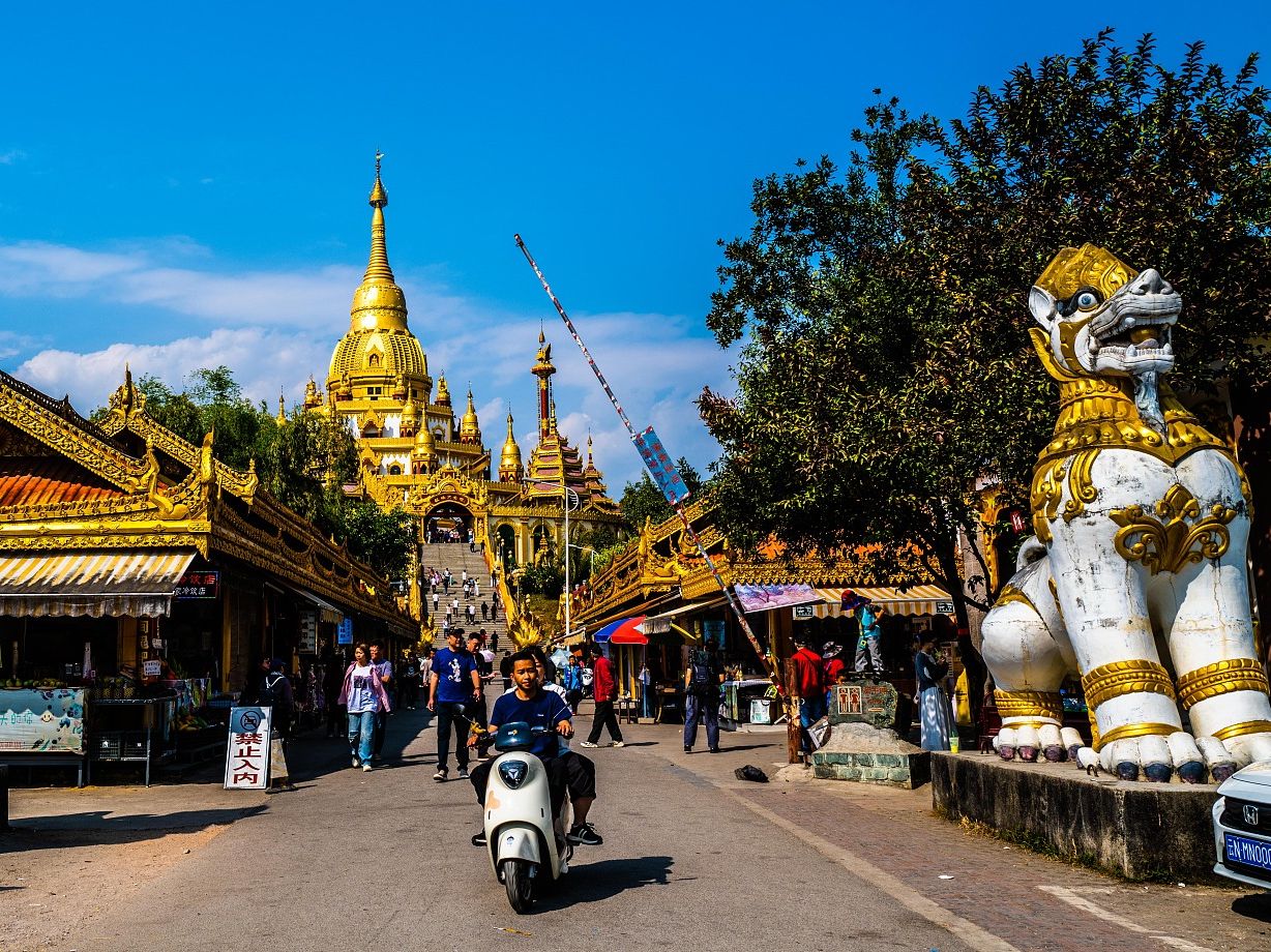 Scooters drive by entrance to Silver Pagoda in Mangshi, Yunnan province