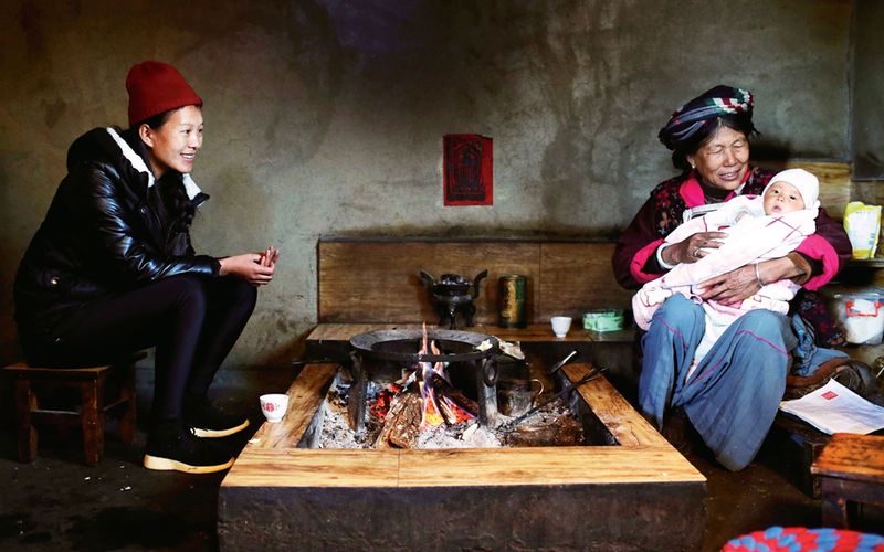 A Mosuo family relaxes as a grandmother holds her grand kid.