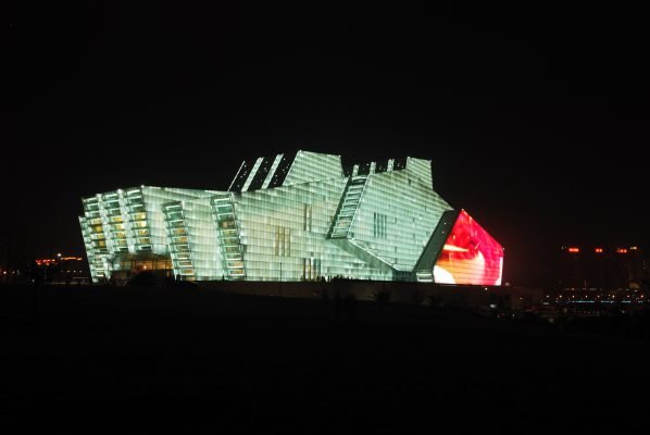 The grayish-green walls of the theater brighten up the night sky.