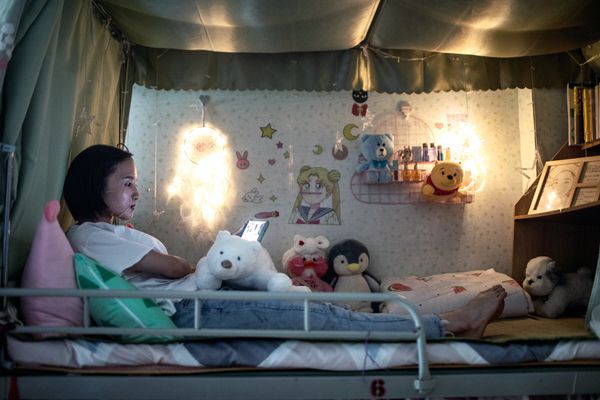 A young Chinese factory worker lays on her bunkbed as she applies a face mask at night. 
