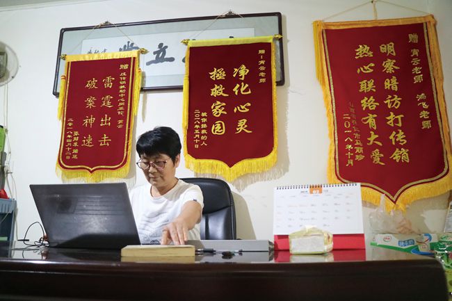 Red banners with warnings about chuanxiao hang behind a woman&#x27;s desk. 