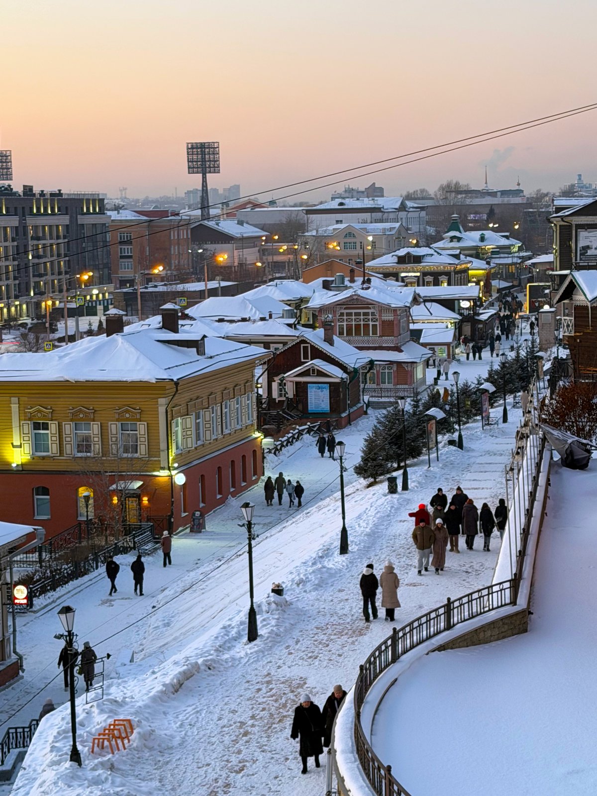 The wooden Siberian-style houses, snowy hills, and pedestrian street resemble Irkutsk’s historic 130th Quarter (Irkutsk Sloboda) area. The winter setting also aligns with its proximity to Lake Baikal,