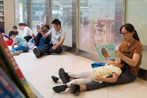 A Chinese mother and her child sit on the floor while reading a book at a bookstore. 