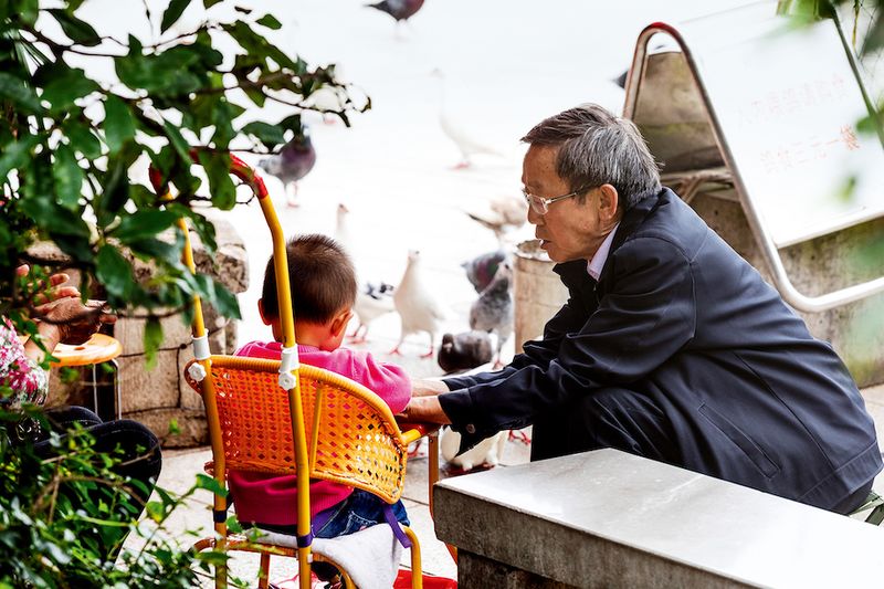 An old Chinese man takes cares of his grandson at a park