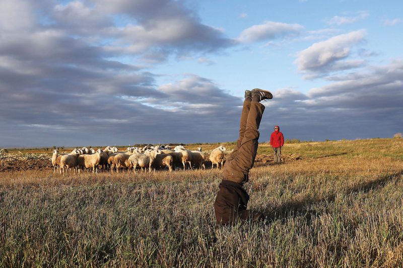 A villager strikes a headstand on the pasture outside of Yugouliang