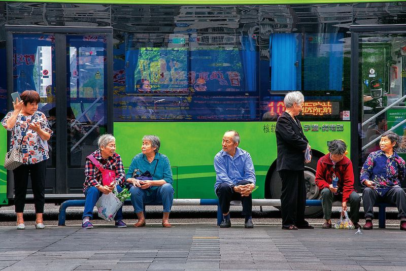 Chinese seniors sitting at a bus stop while chatting with friends