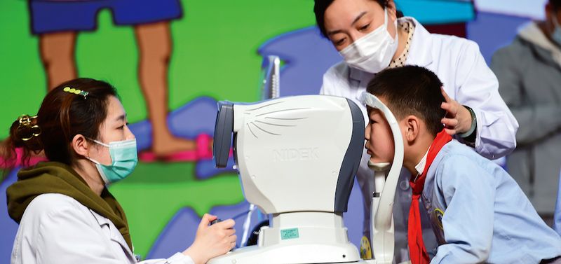 A young Chinese student has eyes checked by two optometrists
