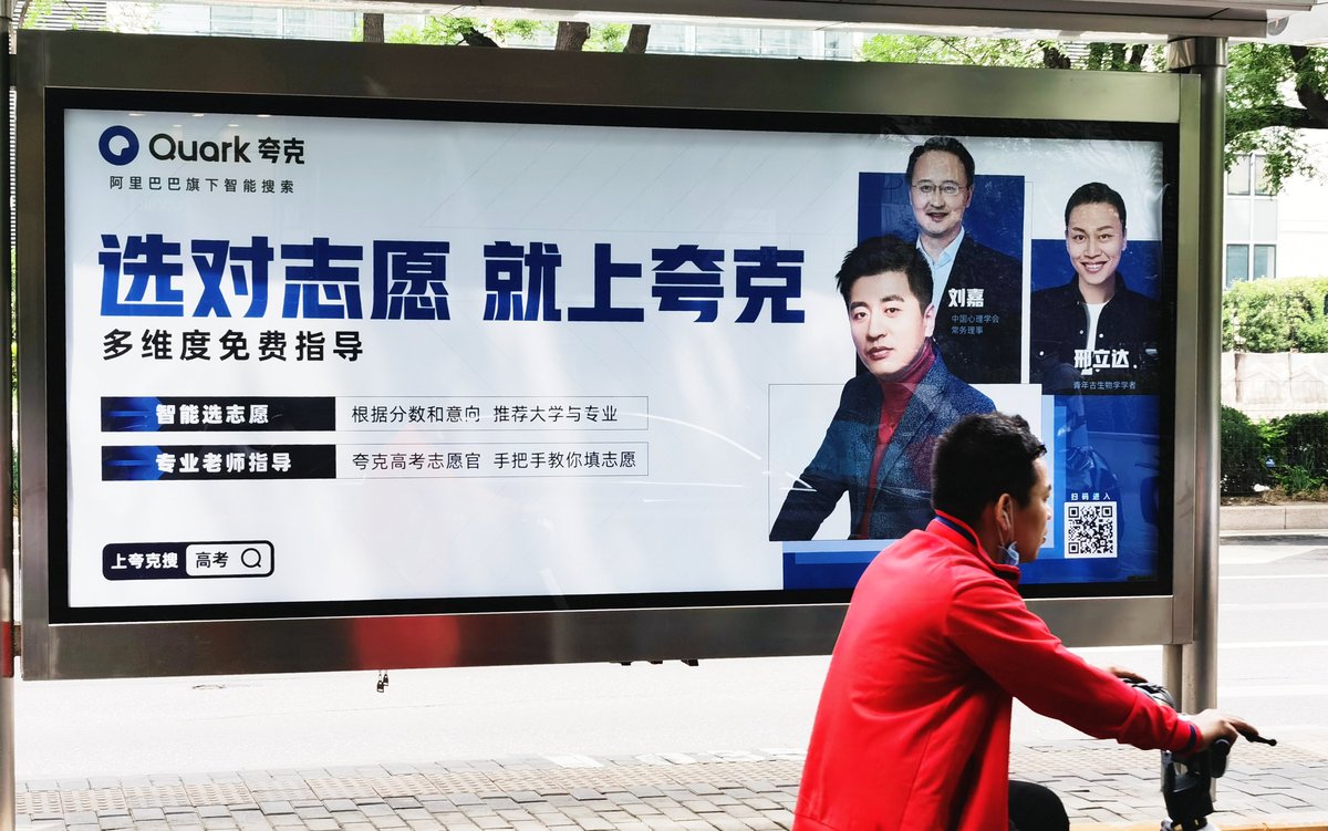 A Chinese bicyclist rides by an advertisement for Alibaba education consultation platform Quark