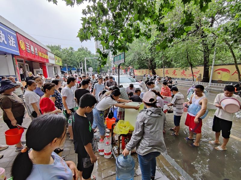 Zhengzhou residents line up to collect drinking water and other donated supplies. (VCG)
