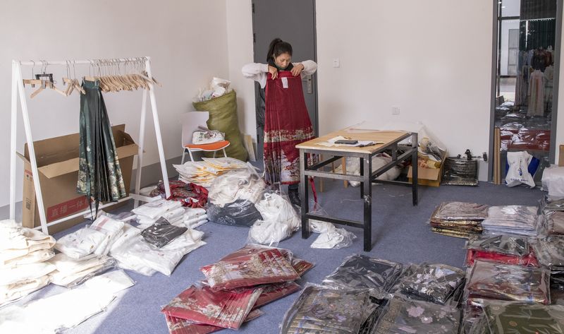A woman organizes hanfu clothing in a showroom in Caoxin