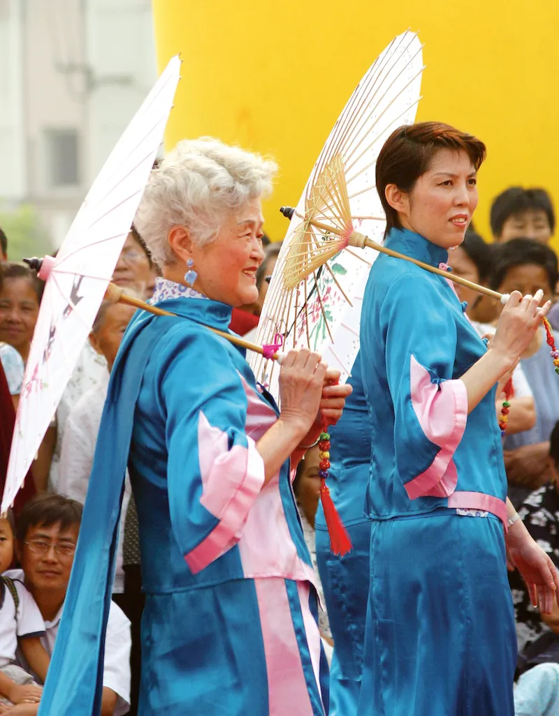 A Chinese senior holds her umbrella while wearing a turquoise outfit