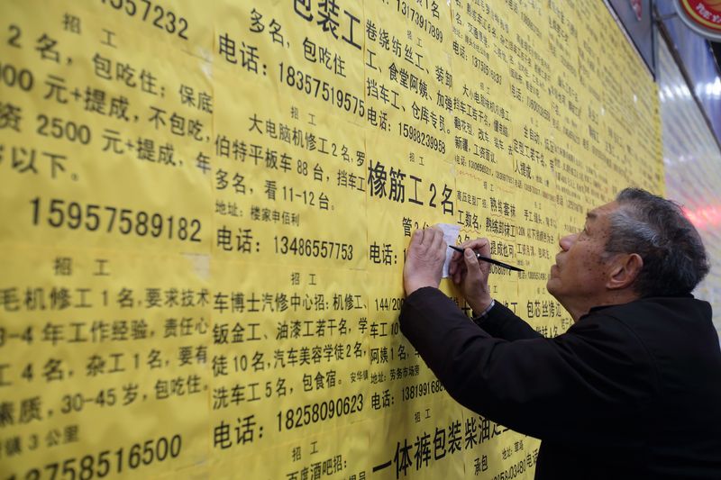 An elderly migrant worker copying down phone numbers at a job fair in Zhejiang province