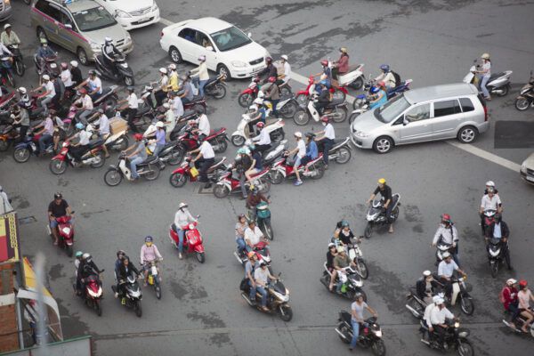 Electronic bikes and electric scooters merge with traffic at a busy intersection. 