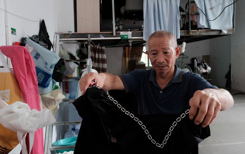 Wang the 69-year-old factory owner shows sample clothes in his factory in Lujiang village, Guangzhou, June 10, 2023.