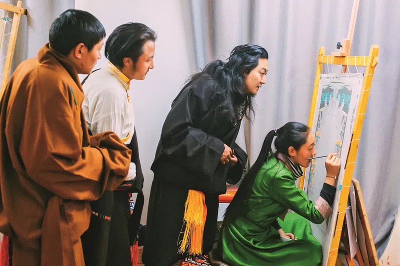 Tibetan thangka art master Karma Tenzin examines his student's project, thangka silk art.