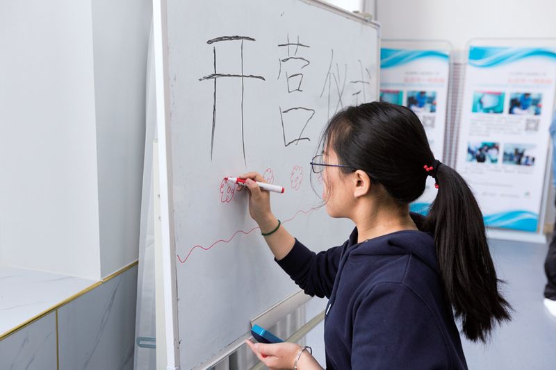Tong Can, concentrates as she write out large Chinese characters and draws small, pink flowers on a whiteboard.