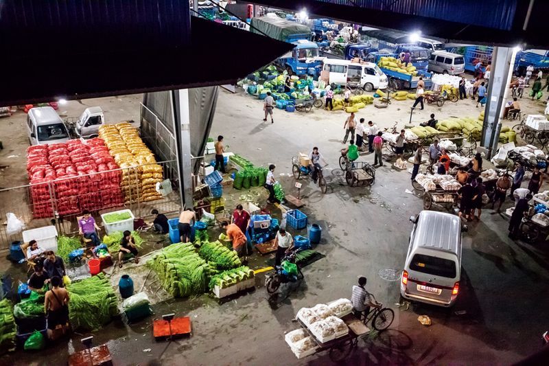 Buyers, sellers, and deliverymen gather in the vegetable market to get goods to market before sunrise