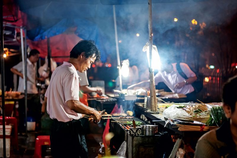 A man cooks meat behind the hearth of his barbecue stall