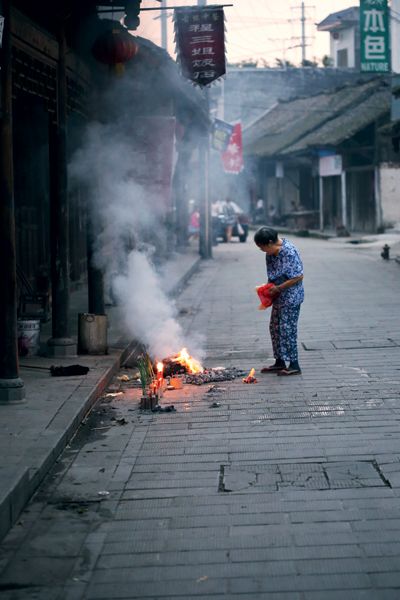 An elderly woman burning paper goblets for her deceased family members at sunset in Huaiyuan Town