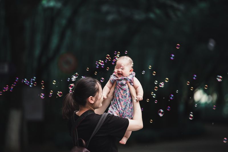 Mom holding baby in the air with bubbles floating around (Unsplash)