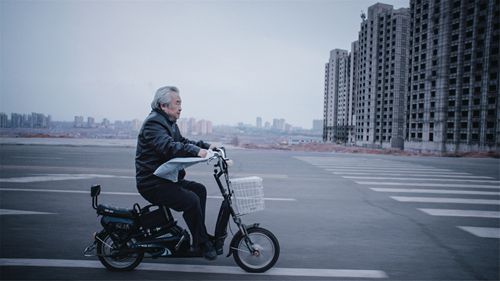 Old Yang (Tumen) motors past a background of still-empty apartment buildings and construction sites in Ordos— remnants of the burst bubble of the “ghost city”phenomenon